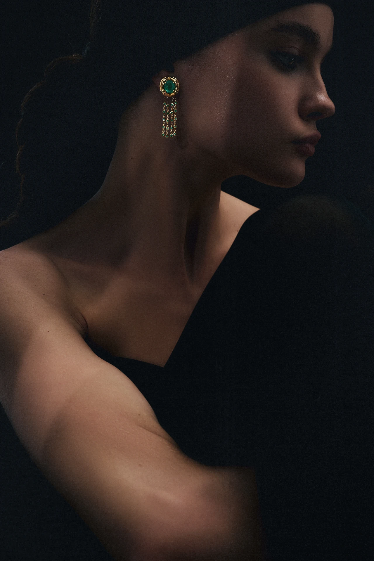 Editorial ORIGEM — brinco pendente em ouro 18k com esmeralda Belmont oval e franjas de esmeraldas, retrato em perfil sobre fundo escuro