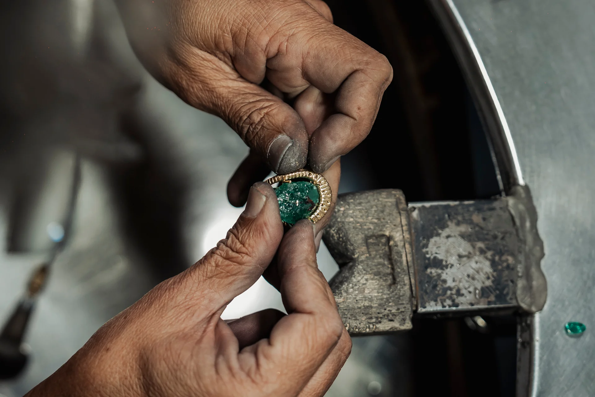 Mãos do mestre joalheiro Raris ajustando engaste à garra de esmeralda Belmont em bigorna do atelier