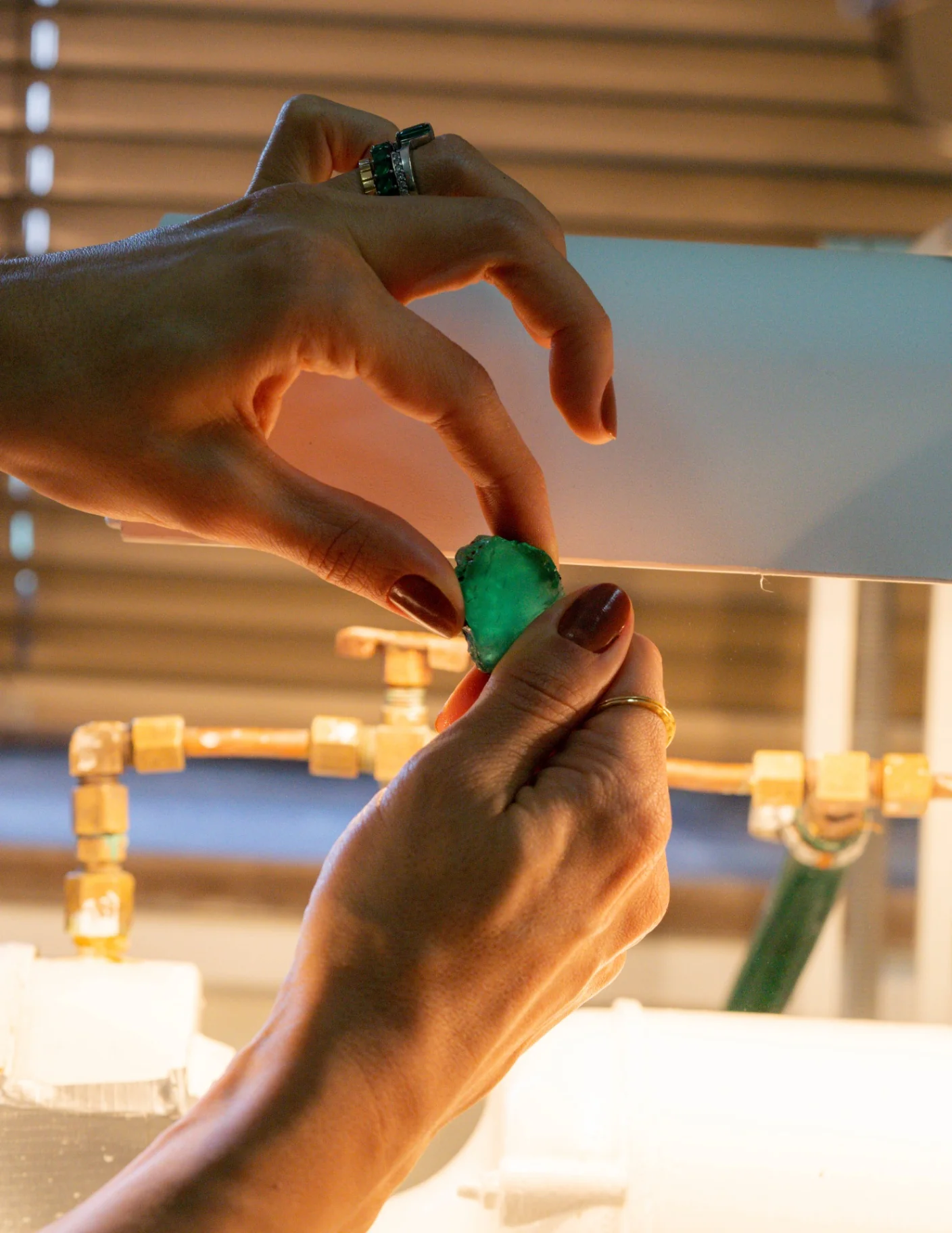 Mão da fundadora Raris segurando esmeralda Belmont bruta sobre bancada de laboratório, com anel de esmeraldas no dedo